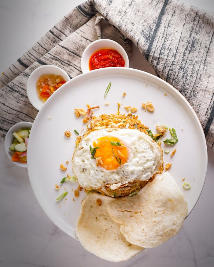 Top view of Nasi Goreng served with a fried egg garnished with herbs, accompanied by sambal and crackers.